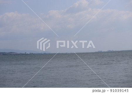 さざ波の湖面の琵琶湖と霞む琵琶湖大橋と街並みと山と雲と青空の風景 さざ波の湖面の琵琶湖と霞む琵琶湖大橋と街並みと山と雲と青空の風景 91039145