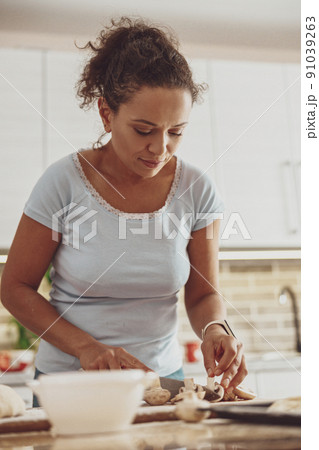 A beautiful woman slices pizza mushrooms on a board standing in her kitchen 91039263