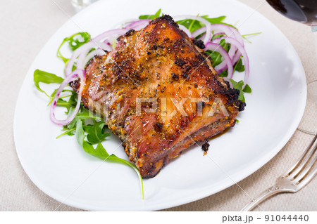 Tasty pork ribs baked under sauce, served with arugula and onion salad 91044440