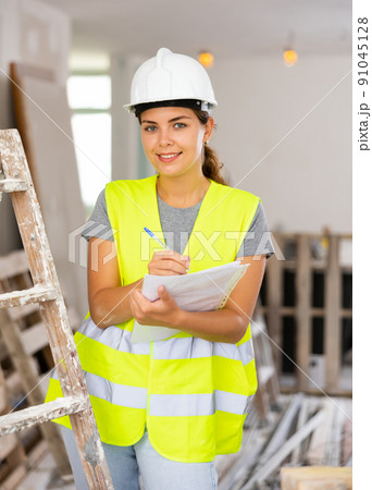 Woman foreman in a protective helmet and yellow vest checks the completed construction work on drawing Woman foreman in a protective helmet and yellow vest checks the completed construction work on drawing 91045128
