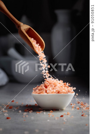 Pink salt in crystals is poured into a small white bowl. Pink salt in crystals is poured into a small white bowl. 91050851