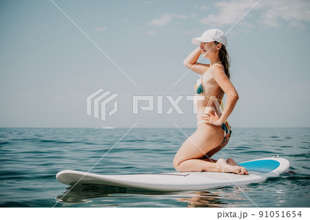 Happy young woman in swimsuit doing yoga on sup board in calm sea, early morning. Balanced pose - concept of healthy life and natural balance between body and mental development 91051654