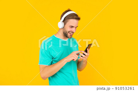 Happy young man texting message on mobile phone listening to digital music in headphones, sms Happy young man texting message on mobile phone listening to digital music in headphones, sms 91053261