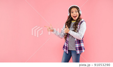 amazed kid listening music in earphones point finger on pink background with copy space, technology 91053290