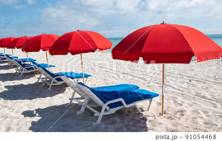 Blue sunloungers and red parasols on sea beach in summer Blue sunloungers and red parasols on sea beach in summer 91054468