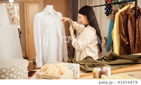 Seamstress in sewing studio, indoors. Beautiful woman, cozy interior. young entrepreneur. photographs finished product Seamstress in sewing studio, indoors. Beautiful woman, cozy interior. young entrepreneur. photographs finished product 91054879