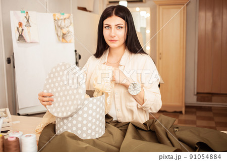 Seamstress in sewing studio, indoors. Beautiful woman, cozy interior. young entrepreneur. looks into camera 91054884