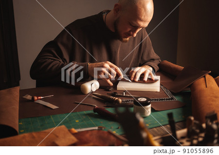Portrait of handsome tanner man at work, small business, authentic workshop, indoors. makes purse 91055896