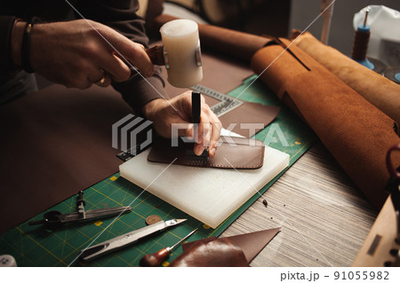 leatherworker beats with hammer. Tanner works with leather, small business, production. 91055982