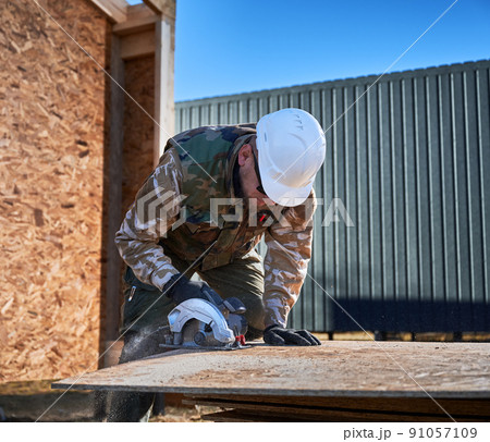 Carpenter using circular saw for cutting wooden OSB board. Man worker building wooden frame house. Carpentry concept. Carpenter using circular saw for cutting wooden OSB board. Man worker building wooden frame house. Carpentry concept. 91057109