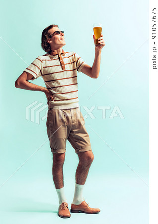 Potrait of young man in casual outfit drinkig cool beer, posing isolated over light blue studio background Potrait of young man in casual outfit drinkig cool beer, posing isolated over light blue studio background 91057675