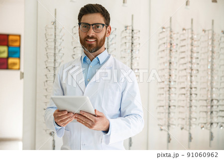 Handsome ophthalmologist with digital tablet in front of the showcase with eyeglasses Handsome ophthalmologist with digital tablet in front of the showcase with eyeglasses 91060962