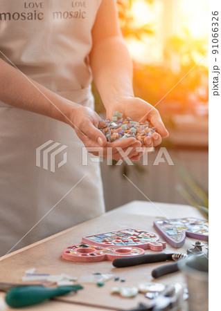Workplace of the mosaic master: women's hands holding mosaic details in the process of making a mosaic 91066326