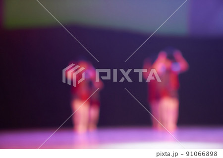Silhouettes of small dancers in red suits. Colored blurred background of the dance festival. Bright stage lighting. High quality photo 91066898