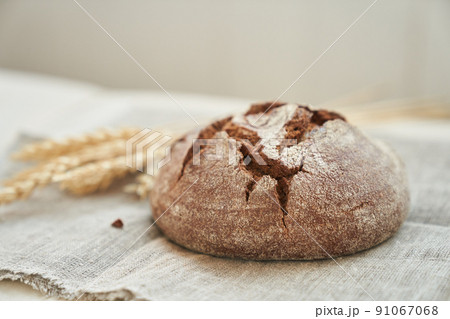 Freshly baked rye bread on a yeast-free starter and on a mixture of whole grain, rye and wheat flour. It lies on a napkin, next to a dried flower with grains. Selective focus. High quality photo 91067068