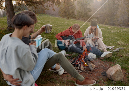 Cheerful friends hanging out together at nature and fire with guitar playing and singing. 91069321