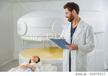 Radiologist controls MRI or CT or PET Scan with female patient undergoing procedure 91070527