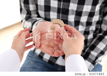The doctor gives the hearing aid to the man, close up The doctor gives the hearing aid to the man, close up 91072883
