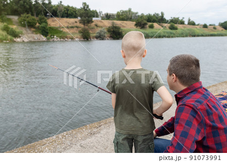 Father and son fishing. Dad shows his son how to hold the spinning and spin the reel. Fishing training on a pond or river. Caring parent concept. 91073991