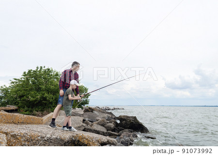 Father and son fishing. Dad shows his son how to hold the spinning and spin the reel. Fishing training on a pond or river. Caring parent concept. 91073992