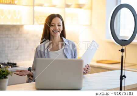 Woman with papers smiling at laptop 91075583