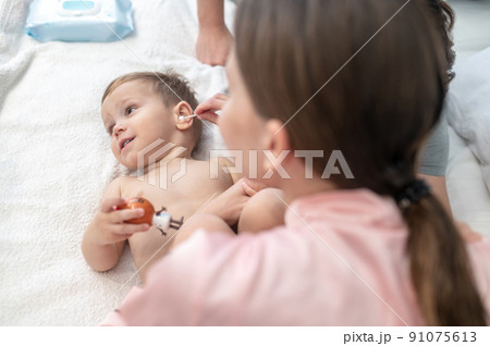Woman cleaning ear of child lying on bed 91075613