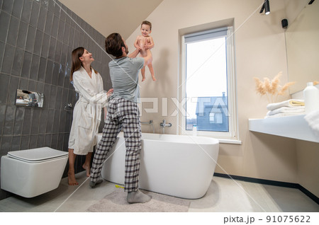 Man holding baby over bathtub and smiling woman 91075622