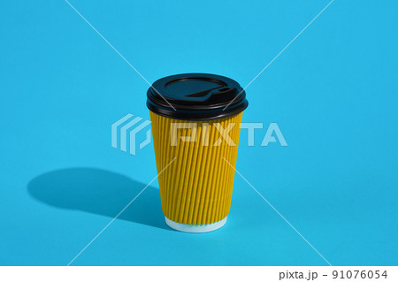 Hot coffee in yellow paper cup with black lid on blue background 91076054