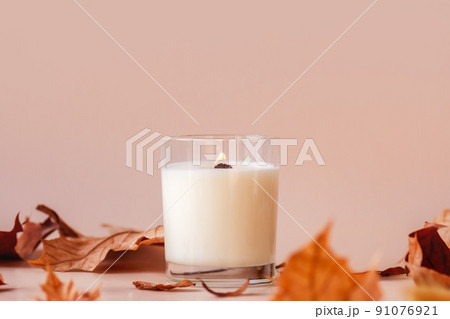 Burning vanilla candle on beige background. Warm aesthetic autumn composition with and dry leaves and flowers. Home comfort, spa, relax and wellness concept. Interior decoration 91076921