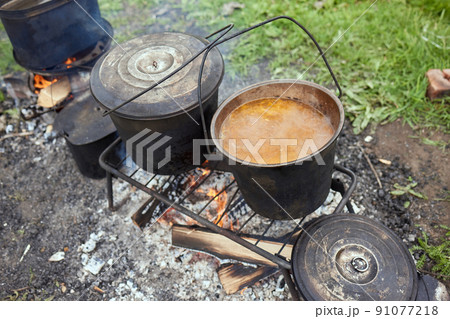 Hiking pot, Bowler in the bonfire. in cauldron at the stake. Traveling, tourism, picnic cooking, cooking at the stake in a cauldron, fire and smoke. Hiking pot, Bowler in the bonfire. in cauldron at the stake. Traveling, tourism, picnic cooking, cooking at the stake in a cauldron, fire and smoke. 91077218