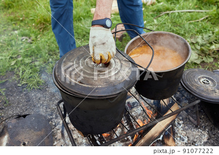 Hiking pot, Bowler in the bonfire. in cauldron at the stake. Traveling, tourism, picnic cooking, cooking at the stake in a cauldron, fire and smoke. Hiking pot, Bowler in the bonfire. in cauldron at the stake. Traveling, tourism, picnic cooking, cooking at the stake in a cauldron, fire and smoke. 91077222