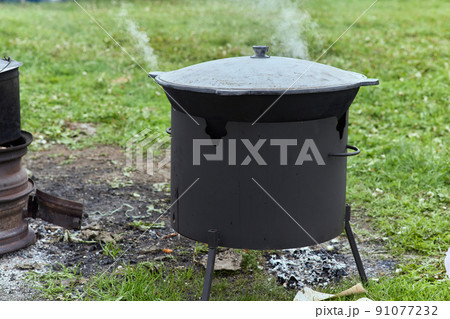 Hiking pot, Bowler in the bonfire. in cauldron at the stake. Traveling, tourism, picnic cooking, cooking at the stake in a cauldron, fire and smoke. 91077232