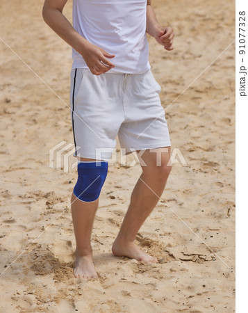 A man pulls a knee pad on her leg before training in the gym after an injury. Isolated on gray background. 91077328