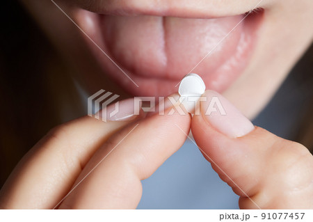 Close up of face of young woman taking drug. The drug addict is standing and putting a pill into her mouth. 91077457