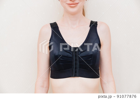 A young woman in black compression underwear after mammoplasty. 91077876