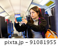 Woman taking photos with smartphone through window glass while travelling by train 91081955