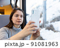 Woman enjoying journey in train, taking pictures on cellphone 91081963