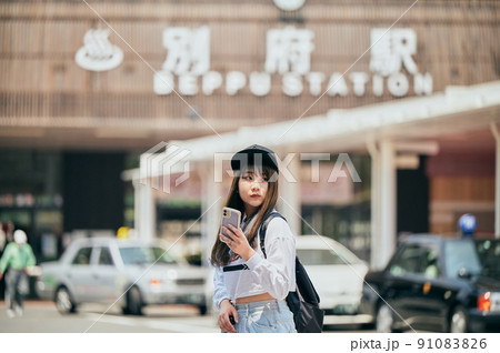 別府駅前でスマホを持って観光する若い女性 91083826