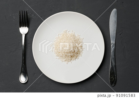Heap of dry rice in a bowl on black background, lack of food, hunger concept Heap of dry rice in a bowl on black background, lack of food, hunger concept 91091583
