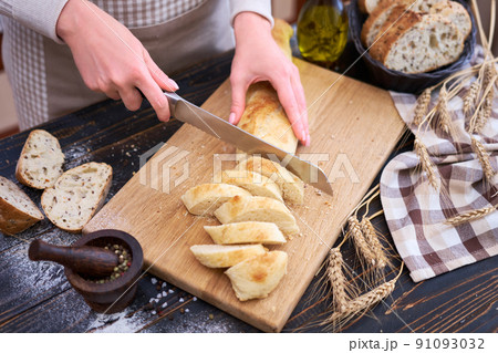 Woman cutting freshly baked bread at wooden kitchen table 91093032
