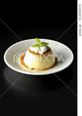 平らなお皿にに盛り付けてある生クリーム、ミントの葉が乗った昔ながらのレトロプリンを黒背景で撮影 平らなお皿にに盛り付けてある生クリーム、ミントの葉が乗った昔ながらのレトロプリンを黒背景で撮影 91099059