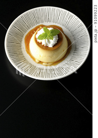 平らなお皿にに盛り付けてある生クリーム、ミントの葉が乗った昔ながらのレトロプリンを黒背景で俯瞰撮影 平らなお皿にに盛り付けてある生クリーム、ミントの葉が乗った昔ながらのレトロプリンを黒背景で俯瞰撮影 91099223