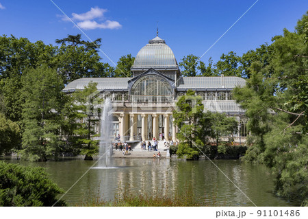 Crystal Palace. Building located in the Retiro Park in Madrid with its glass windows surrounded by trees and green vegetation on a sunny day and some clouds in the sky, in Spain. Europe. Photography. Crystal Palace. Building located in the Retiro Park in Madrid with its glass windows surrounded by trees and green vegetation on a sunny day and some clouds in the sky, in Spain. Europe. Photography. 91101486