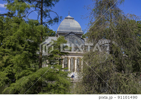Crystal Palace. Building located in the Retiro Park in Madrid with its glass windows surrounded by trees and green vegetation on a sunny day and some clouds in the sky, in Spain. Europe. Photography. 91101490