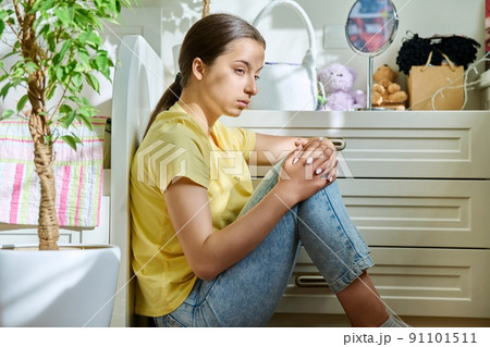 Sad teenage girl sitting on the floor at home 91101511