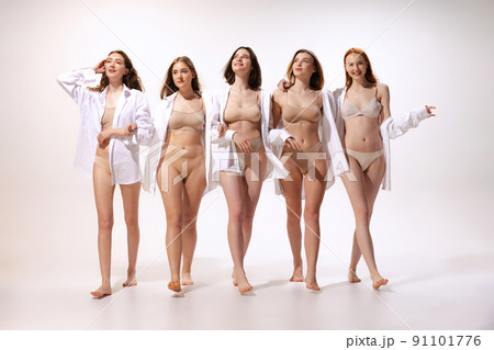 Group of young beautiful women posing in beige cotton underwear and white shirt posing in walk isolated over white studio background 91101776