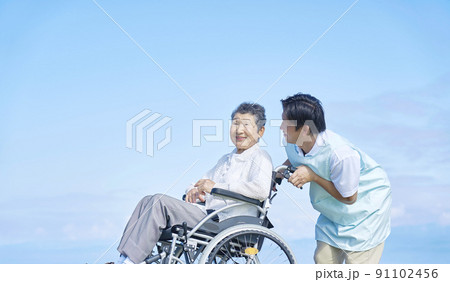 看護師と屋外を車椅子に乗ってお出かけする高齢者女性 91102456