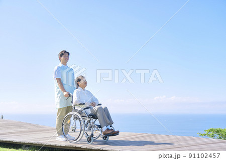 看護師と屋外を車椅子に乗ってお出かけする高齢者女性 91102457
