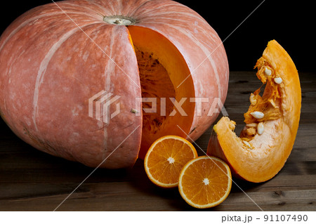 Fresh whole organic pumpkin and sliced, oranges halves on a dark wooden background 91107490