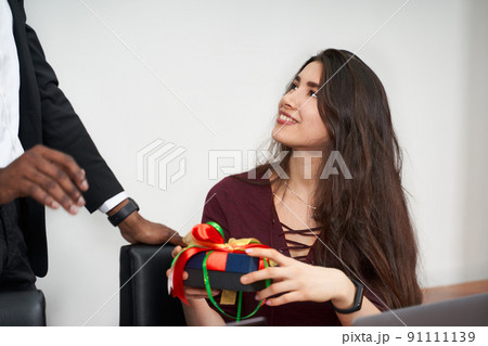 Woman receiving a beautiful gift from her male colleague while working in the office, relationships concept 91111139